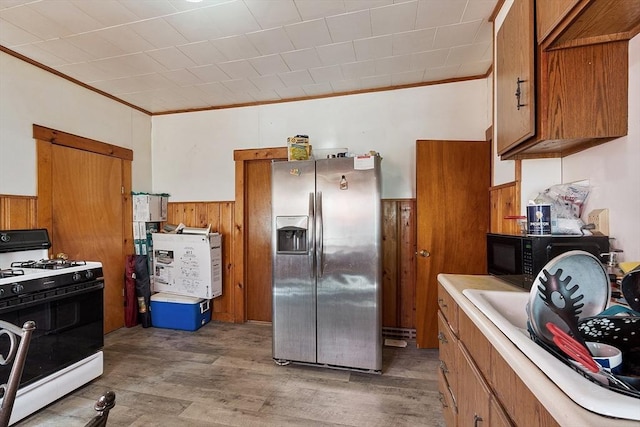kitchen with brown cabinets, stainless steel fridge, black microwave, range with gas cooktop, and ornamental molding