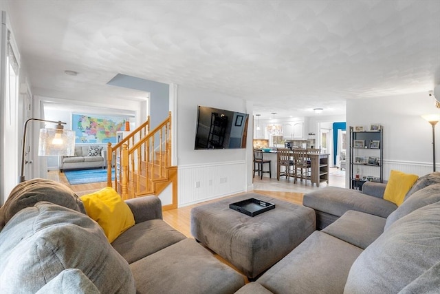 living area featuring light wood-style floors, stairs, and a wainscoted wall