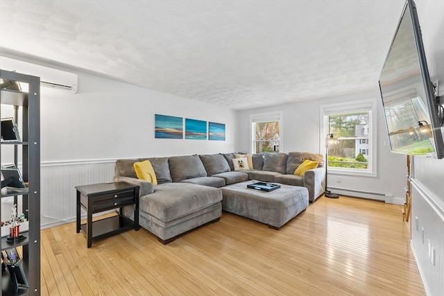 living room featuring light wood-style floors, baseboard heating, and a wall mounted air conditioner