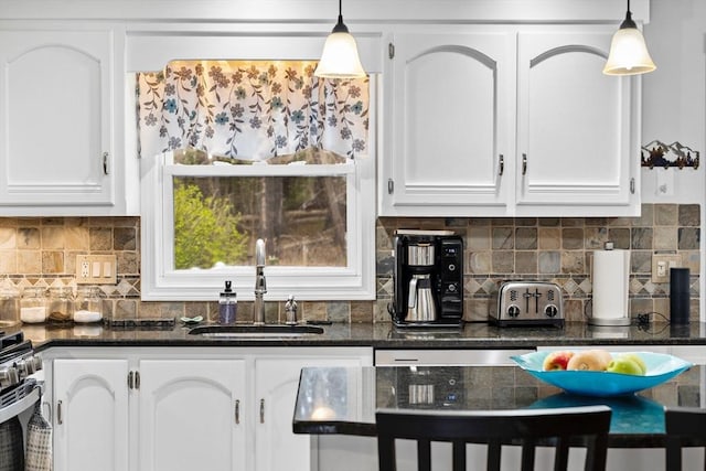 kitchen featuring white cabinets, a sink, dark stone countertops, decorative light fixtures, and decorative backsplash