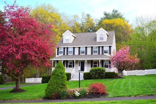 view of front facade with a porch, a shingled roof, fence, and a front yard