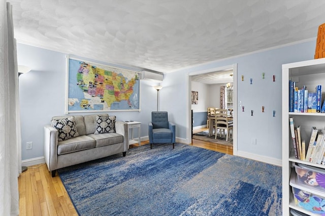 living room with a wall unit AC, baseboards, a notable chandelier, ornamental molding, and hardwood / wood-style floors
