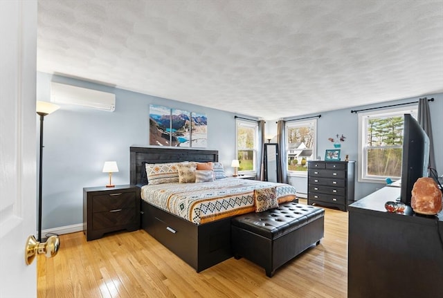 bedroom with light wood-style floors, a textured ceiling, baseboards, a baseboard radiator, and a wall mounted AC