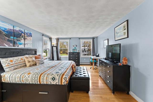 bedroom featuring baseboards, light wood-style flooring, and a baseboard radiator
