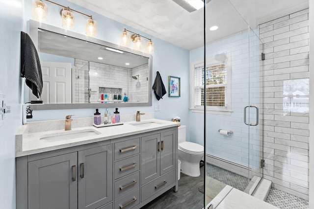 full bathroom with double vanity, toilet, a sink, and a stall shower