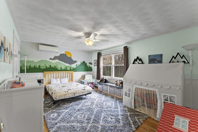 bedroom with an AC wall unit, a textured ceiling, ceiling fan, and wood finished floors
