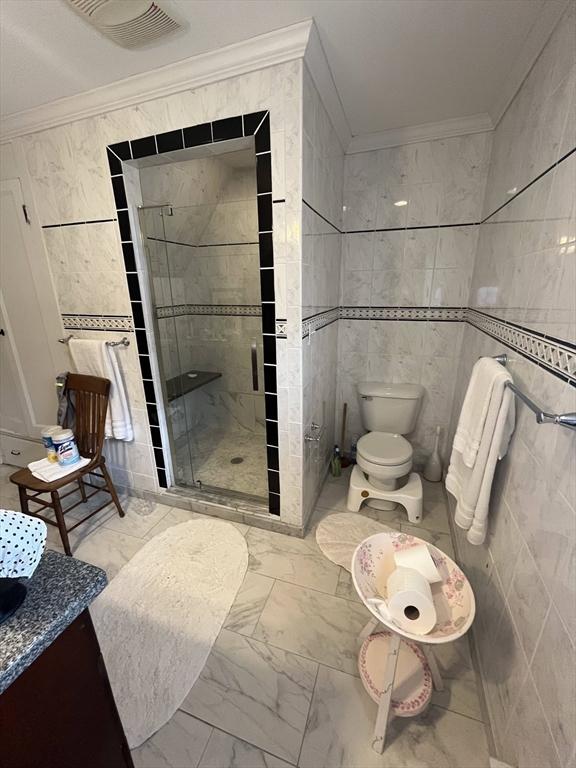 bathroom featuring marble look tiles, tile walls, a shower stall, ornamental molding, and toilet