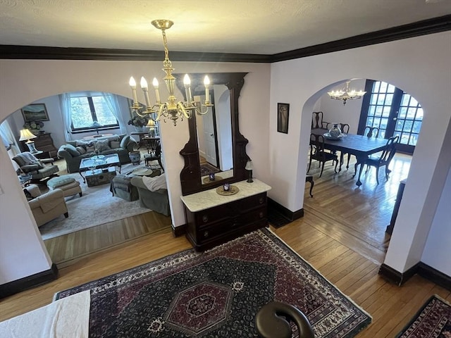 hall with arched walkways, a chandelier, ornamental molding, wood-type flooring, and baseboards