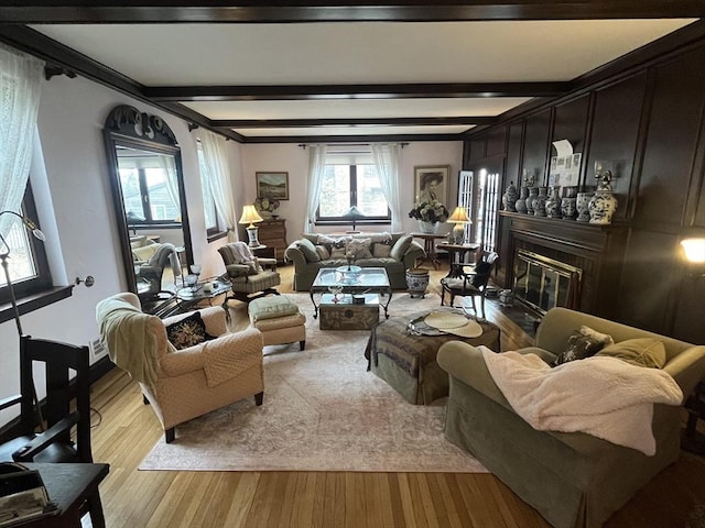 living area featuring a glass covered fireplace, wood finished floors, beam ceiling, and crown molding