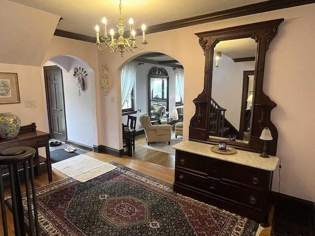 foyer with arched walkways, wood finished floors, a chandelier, crown molding, and baseboards