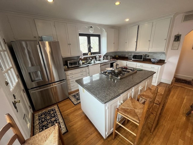 kitchen with appliances with stainless steel finishes, light wood finished floors, white cabinets, recessed lighting, and a kitchen island