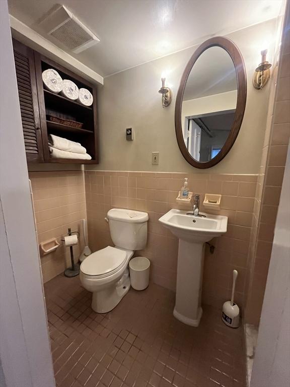 half bathroom featuring tile walls, tile patterned flooring, toilet, a wainscoted wall, and a sink