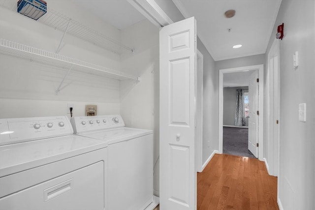 clothes washing area with light wood-type flooring, crown molding, and washing machine and clothes dryer