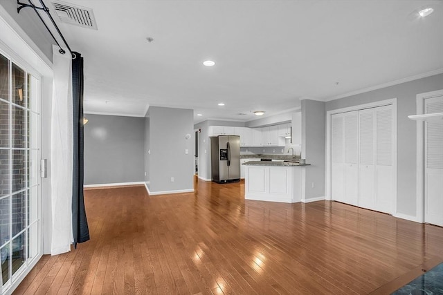 unfurnished living room featuring sink, wood-type flooring, and ornamental molding