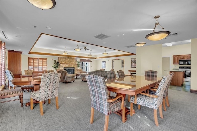 carpeted dining space with a stone fireplace and a tray ceiling