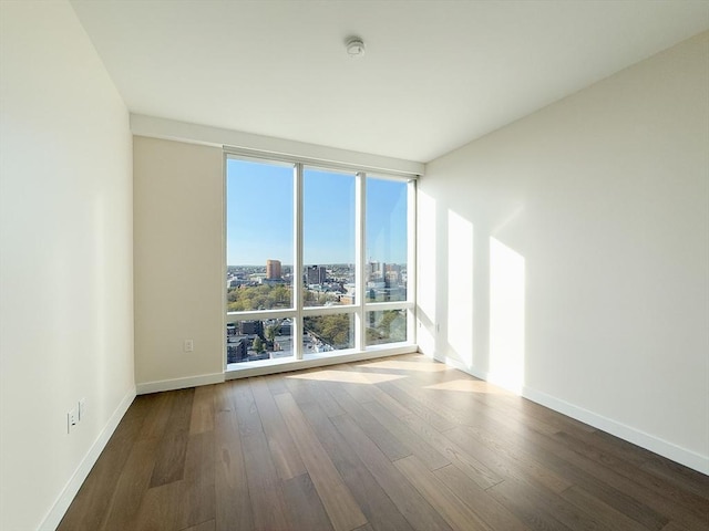 spare room with a wall of windows, wood finished floors, baseboards, a view of city, and a smoke detector