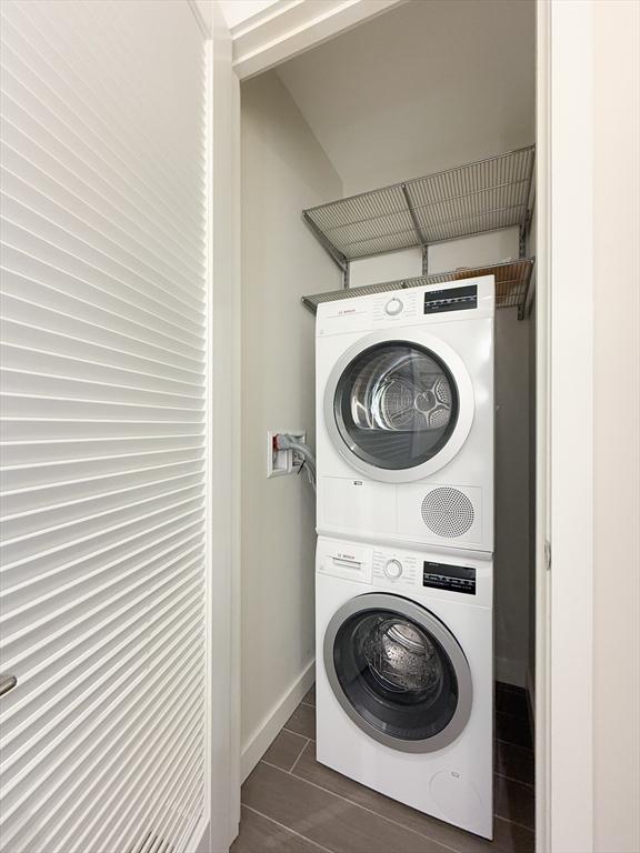 laundry room featuring stacked washer / dryer, baseboards, and wood tiled floors