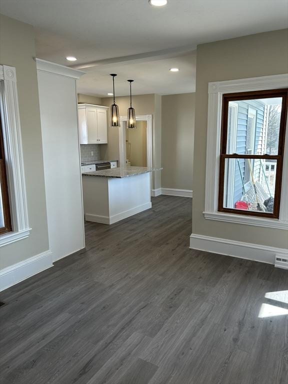 kitchen with backsplash, a kitchen island, dark wood-type flooring, baseboards, and white cabinets