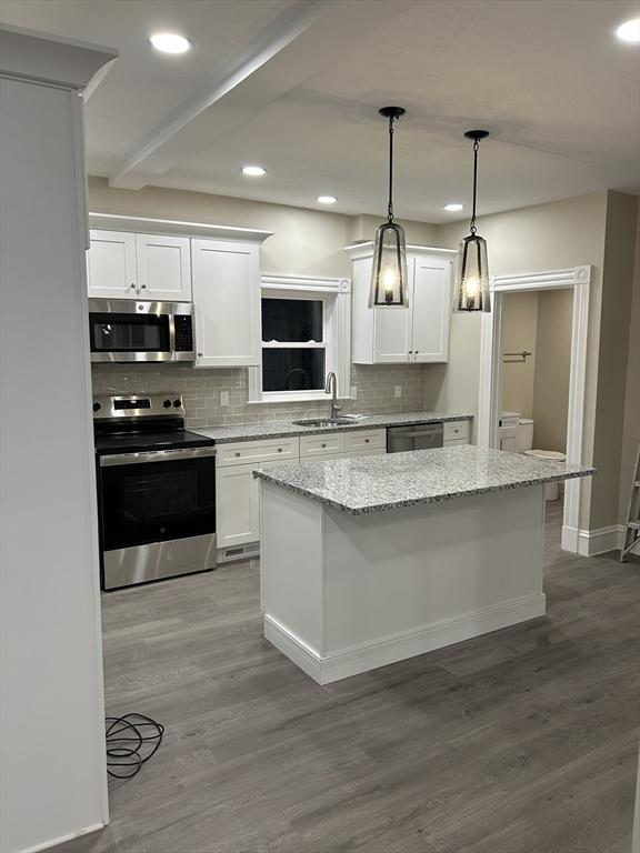 kitchen featuring a kitchen island, a sink, stainless steel appliances, dark wood-type flooring, and white cabinetry