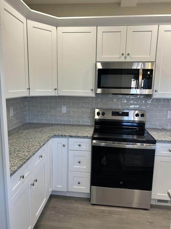 kitchen with white cabinetry, decorative backsplash, wood finished floors, and stainless steel appliances