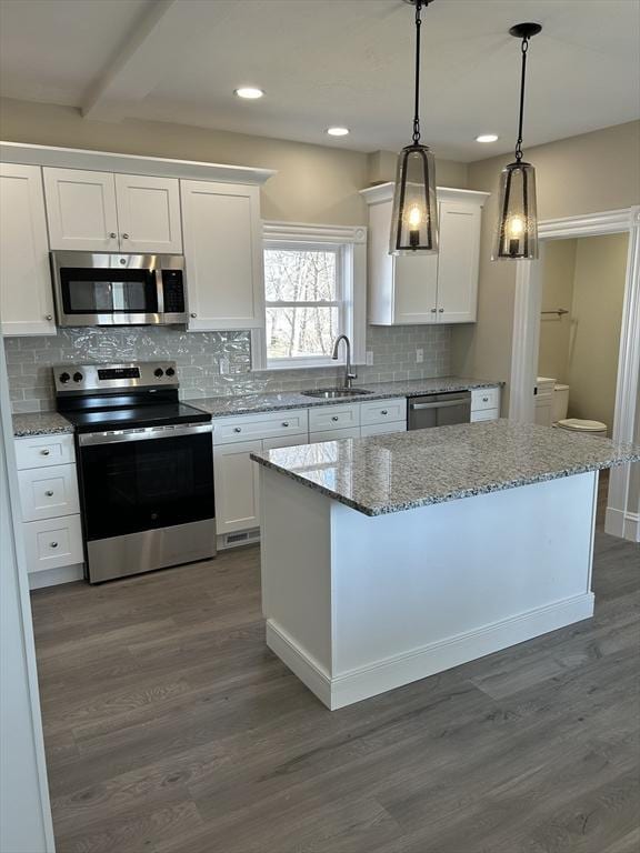 kitchen with a sink, a kitchen island, stainless steel appliances, white cabinetry, and dark wood-style flooring