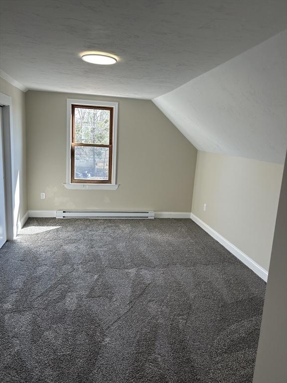 additional living space with baseboards, a textured ceiling, and dark carpet