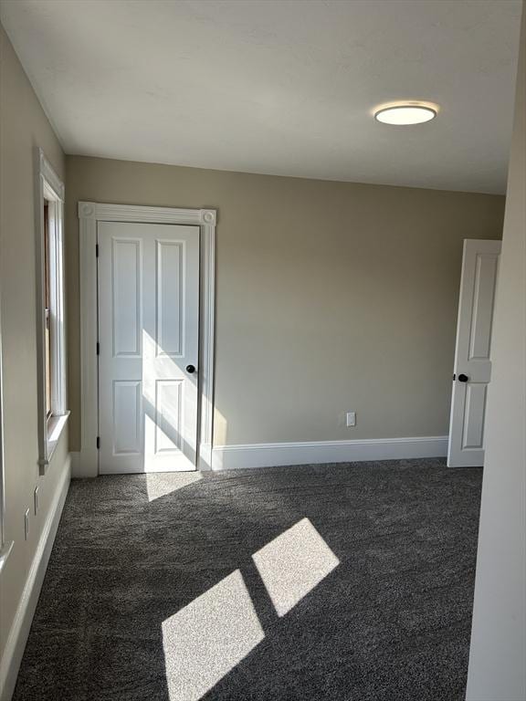 spare room featuring baseboards and dark colored carpet