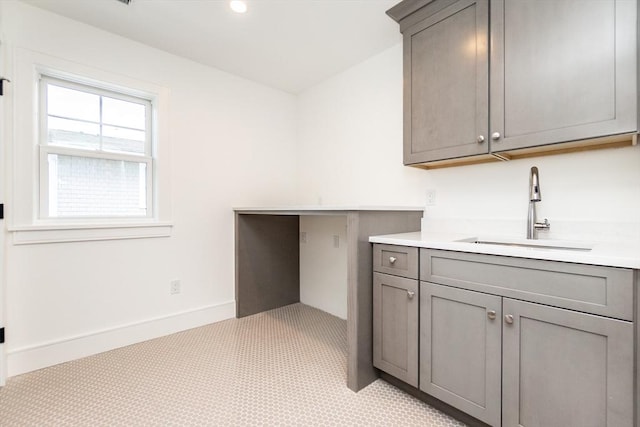 kitchen featuring baseboards, light countertops, a sink, and gray cabinetry