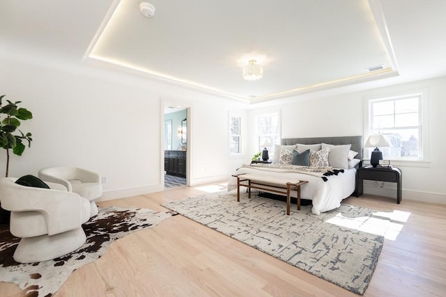 bedroom featuring a raised ceiling, visible vents, ensuite bathroom, wood finished floors, and baseboards