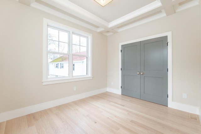 unfurnished bedroom with beam ceiling, a closet, light wood-style flooring, coffered ceiling, and baseboards