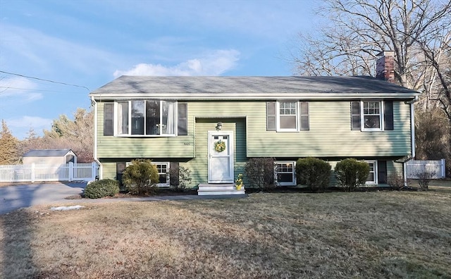 bi-level home featuring a chimney, a front yard, fence, and a gate