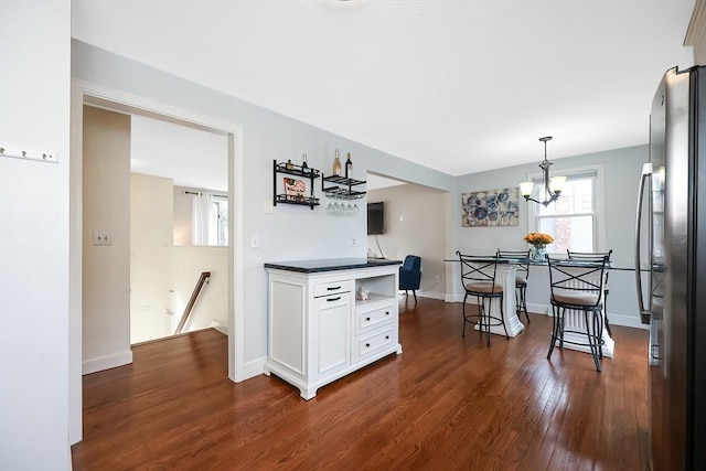 kitchen featuring dark wood-style flooring, hanging light fixtures, freestanding refrigerator, white cabinets, and baseboards