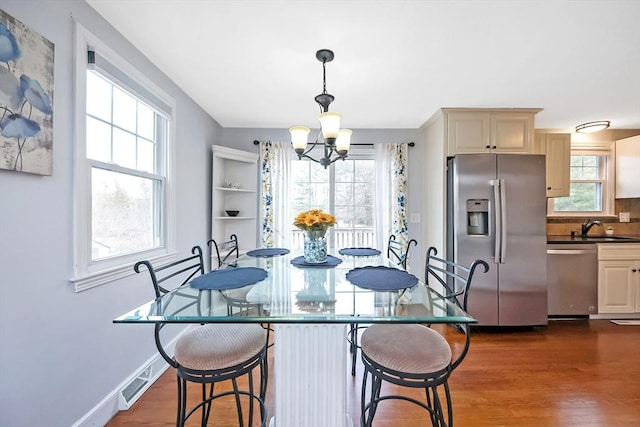 dining space with dark wood-style floors, a notable chandelier, visible vents, and baseboards