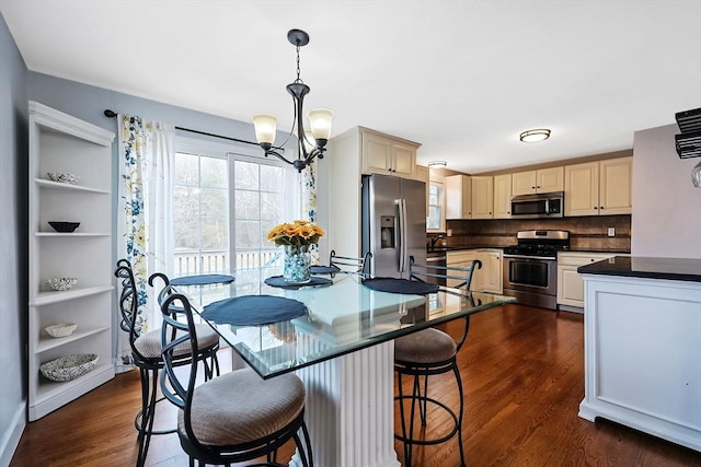 kitchen with stainless steel appliances, dark countertops, tasteful backsplash, cream cabinets, and dark wood-type flooring