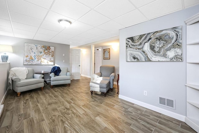 living area featuring baseboards, visible vents, a drop ceiling, and wood finished floors