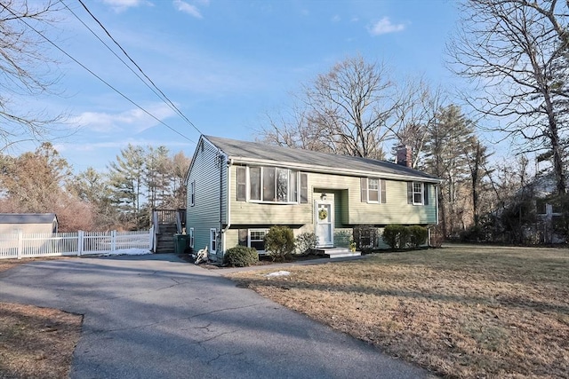 raised ranch with driveway, a chimney, fence, and a front lawn