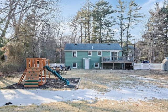 back of house with fence, a deck, and a playground