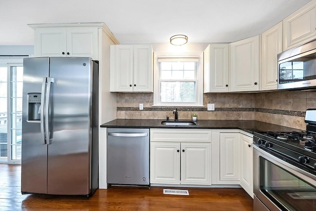 kitchen with tasteful backsplash, white cabinets, dark countertops, stainless steel appliances, and a sink