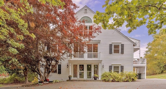 back of house with driveway, a balcony, and a carport