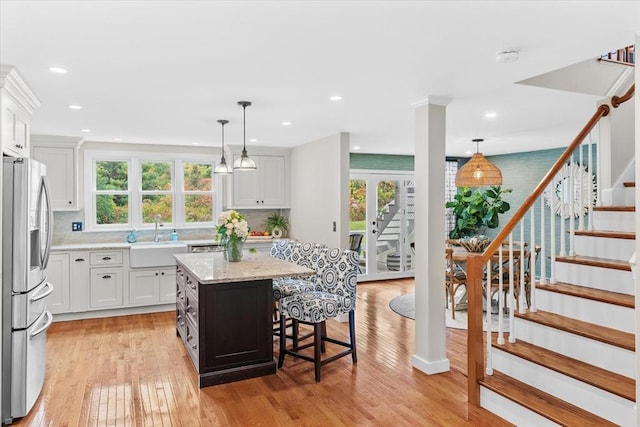 kitchen featuring a sink, white cabinetry, a kitchen bar, a kitchen island, and stainless steel refrigerator with ice dispenser