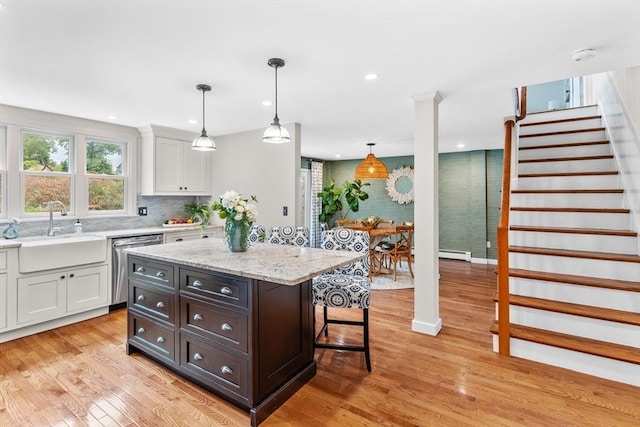 kitchen with white cabinets, a sink, light wood-style flooring, a kitchen bar, and stainless steel dishwasher