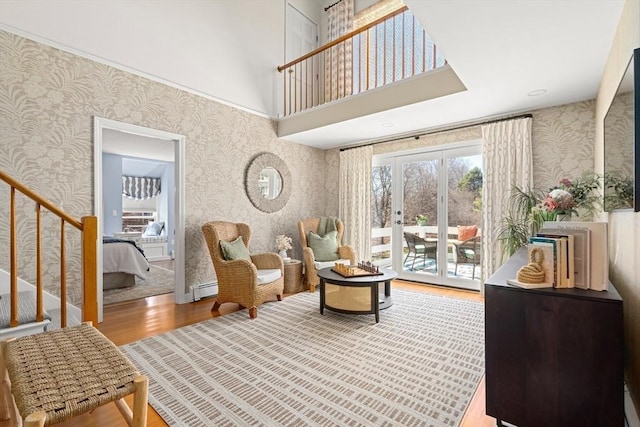 sitting room featuring stairs, wood finished floors, baseboard heating, and wallpapered walls