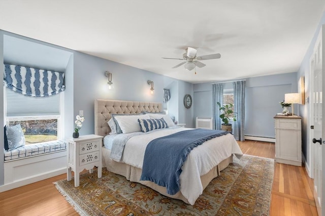 bedroom featuring a ceiling fan, a baseboard heating unit, and light wood finished floors