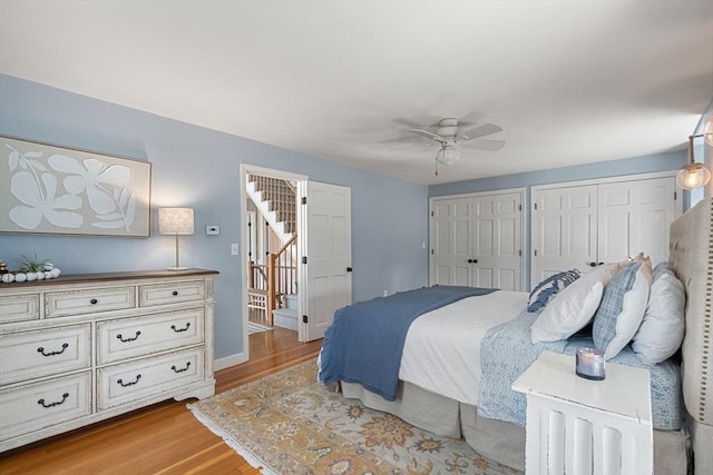 bedroom featuring a ceiling fan, baseboards, multiple closets, and light wood finished floors
