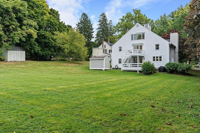 back of house featuring a storage unit, a wooden deck, an outbuilding, a chimney, and a lawn