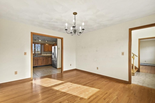 unfurnished room with light hardwood / wood-style flooring, baseboard heating, a notable chandelier, and sink