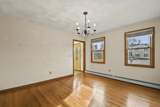 spare room featuring light hardwood / wood-style flooring, baseboard heating, a wealth of natural light, and a notable chandelier