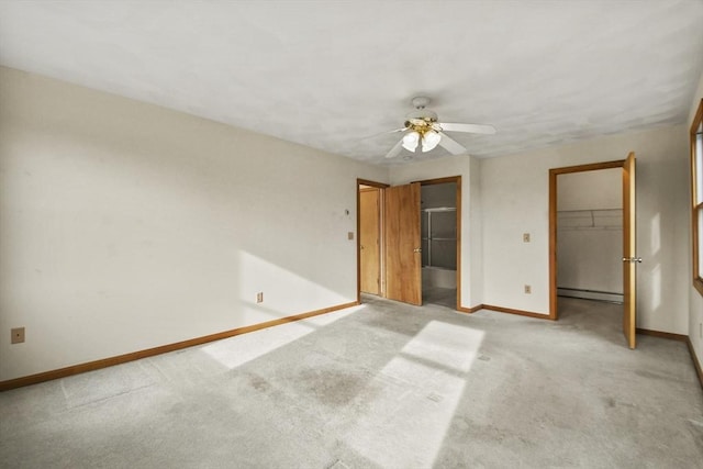 unfurnished bedroom with a walk in closet, light colored carpet, ceiling fan, and a baseboard heating unit