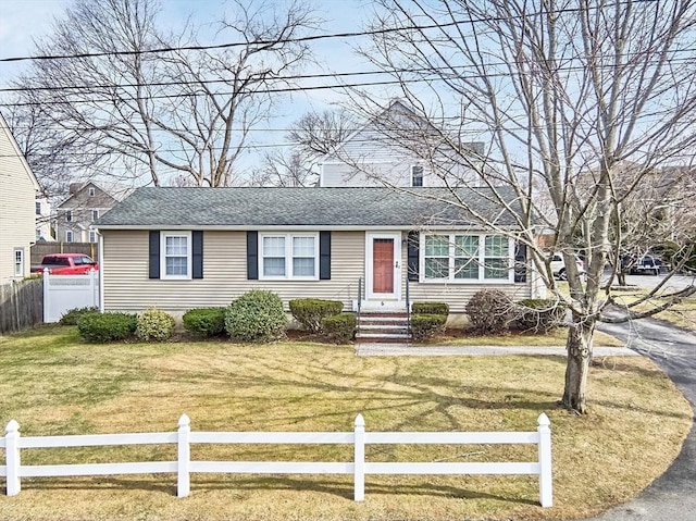 ranch-style house featuring entry steps, a front lawn, a fenced front yard, and a shingled roof