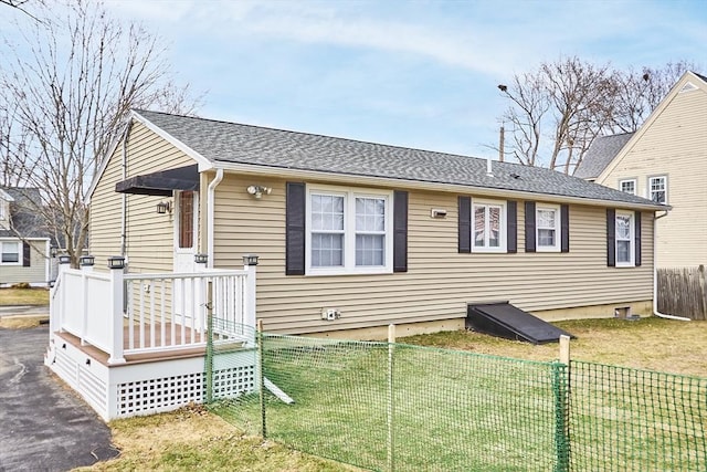 view of front of home featuring a wooden deck, roof with shingles, a front yard, and fence